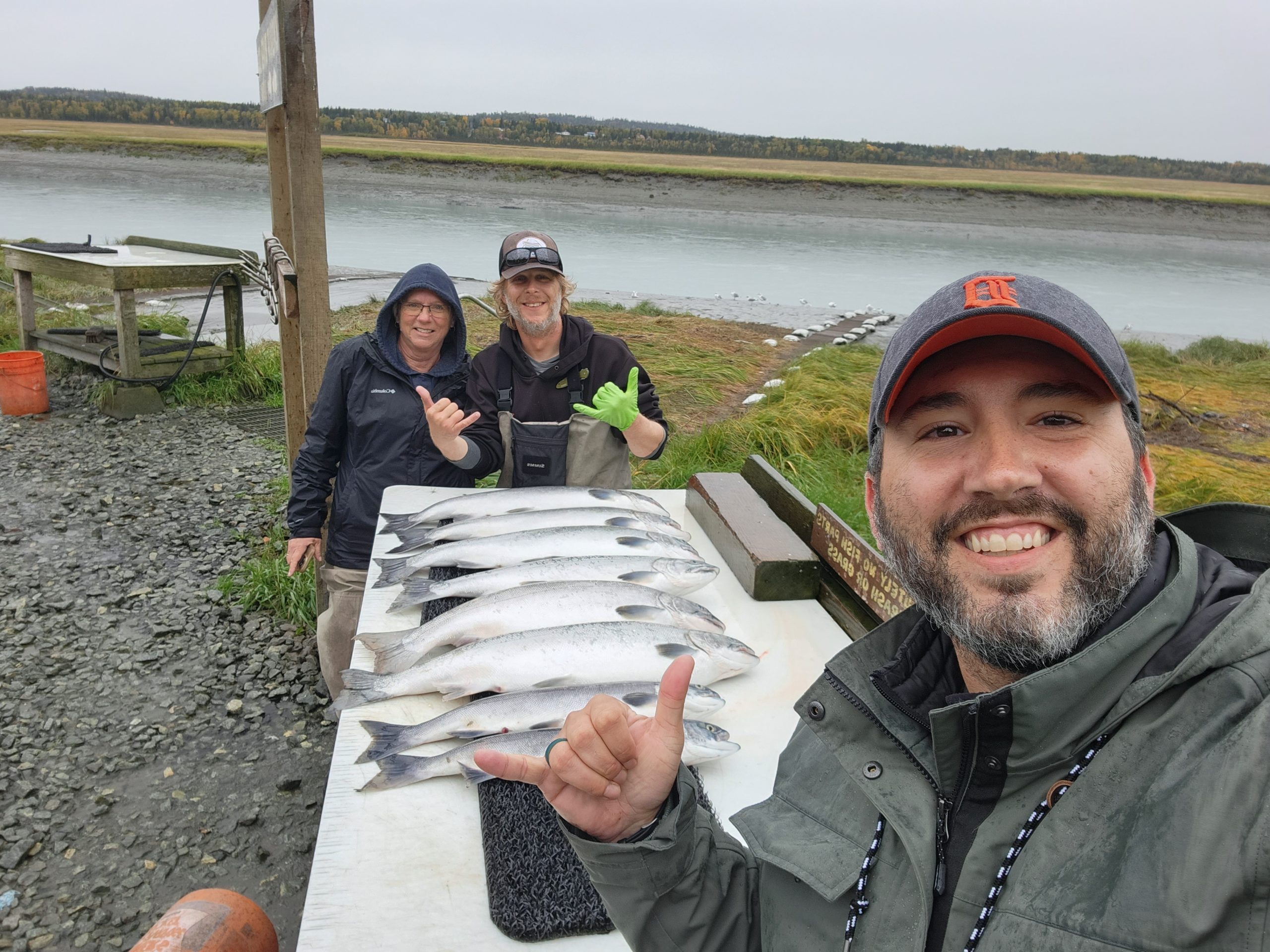 Family of 3 pose together in front of a table of Alaskan fish